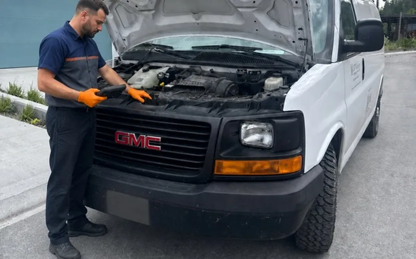 Certified mechanic diagnosing a 2016 GMC Savana work van on-site in Kelowna, hood open, scanner in hand
