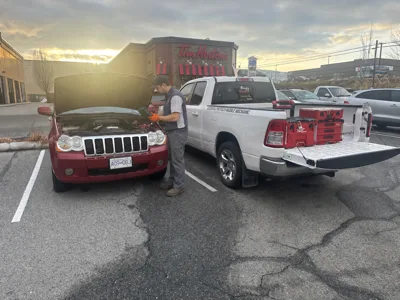 Certified mechanic servicing a Jeep Grand Cherokee on-site in a Kelowna parking lot